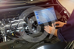 Mechanic Using Laptop While Examining Car Engine photo