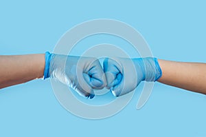 Hands in medical gloves greeting each other with fist bump on blue background.