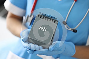 Hands in medical gloves hold 2021 calendar closeup