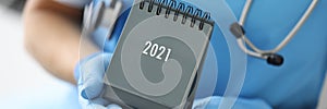 Hands in medical gloves hold 2021 calendar closeup