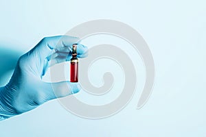 Hands in medical gloves holding syringe and ampoule on blue background. Copy space. Medicine, injections and vaccination concept.