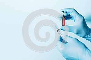Hands in medical gloves holding syringe and ampoule on blue background. Copy space. Medicine, injections and vaccination concept.