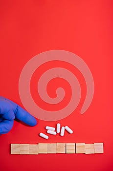 Hands in medical gloves point on wooden blocks on colored red background with medicine pills. Concept book cover medical