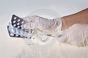 Hands of the medical worker in white gloves holding a syringe and tablets