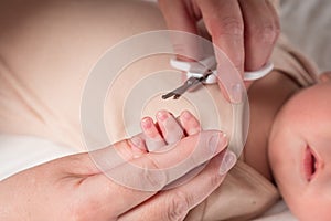Hands of mom cutting tiny baby nails with children scissors
