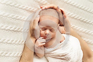 hands of mom and dad hold the head of a newborn baby