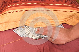 Hands with money hide them under mattress. A man's hand takes money from under the pillow. A man hides money in a bed photo