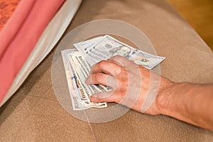 Hands with money hide them under mattress. A man's hand takes money from under the pillow. A man hides money in a bed photo