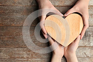 Hands of mother and child holding heart on wooden background