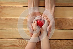 Hands of mother and child holding red heart on wooden background