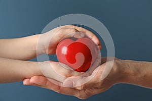 Hands of mother and child with red heart on color background