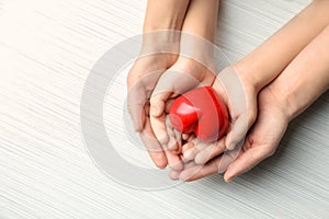 Hands of mother and child with red heart on light background