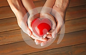 Hands of mother and child with red heart on wooden background
