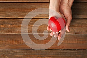 Hands of mother and child with red heart on wooden background