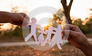 Hands of mother and daughter holding family cut out paper in autumn park on sunset background