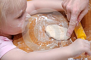 Hands of mother and little daughter knead the dough on a wooden table