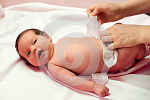 Hands of mother putting on diaper on two weeks old child. Infant baby girl lying with open mouth while mom is changing her nappy