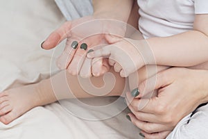 Hands of a mother and a small child, close-up, light colors. Mom hugs the baby. The concept of maternal, parental love and care.
