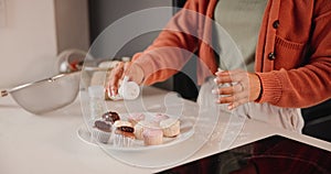 Hands, muffin and person sprinkle sugar powder for baking food, pastry or frosting sweets in home kitchen counter