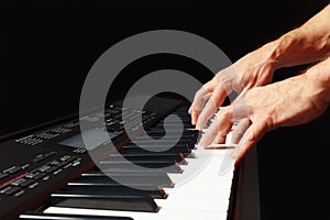 Hands of musician play the keys of the electronic piano on black background