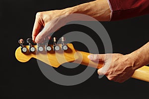 Hands of musician tunes the electric guitar on black background