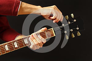 Hands of musician tunes the guitar on dark background