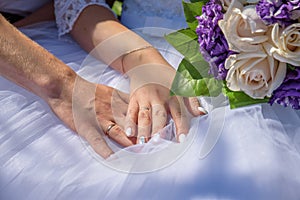 Hands of newly married couple with got on golden rings on wedding dress