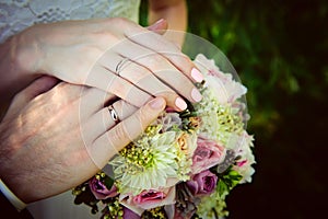 Hands of newlyweds on the background of wedding bouquet. Gold wedding rings on the finger of bride and groom, close-up. Concept