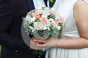 Hands of the newlyweds with a bouquet of the bride close-up. Marriage concept.