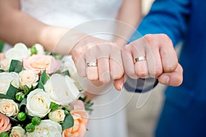 Hands of the newlyweds bride and groom with gold wedding rings close-up on a background of a wedding bouquet of roses