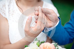 Hands of the newlyweds bride and groom with gold wedding rings close-up on a background of a wedding bouquet of roses