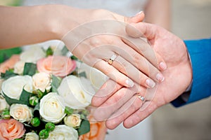 Hands of the newlyweds bride and groom with gold wedding rings close-up on a background of a wedding bouquet of roses