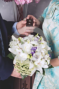 The hands of the newlyweds hold a box-case with gold wedding rings and a bouquet of flowers. A bouquet of white cream roses and