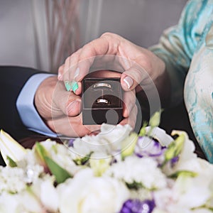 The hands of the newlyweds hold a box-case with gold wedding rings and a bouquet of flowers. A bouquet of white cream roses and