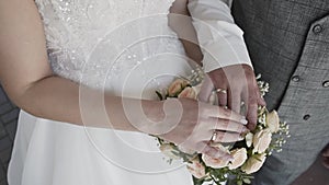 The hands of the newlyweds lie on the wedding bouquet on their hands sparkle bright golden wedding rings