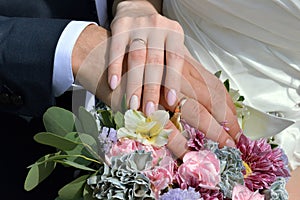 The hands of the newlyweds with rings against the background of a bouquet of flowers.
