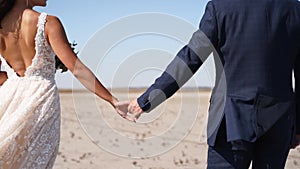 Hands of newlyweds walking together at desert landscape on wedding day. Just married couple in love going holding hands