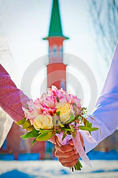 Hands of newlyweds and wedding bouquet on the background of the mosque. Muslim wedding in Russia