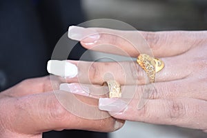 The hands of the newlyweds at the wedding, the groom puts on the wedding gold ring on the finger of the bride
