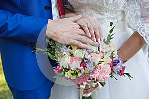 Hands of newlyweds with wedding rings and a bouquet of flowers. The groom in a blue suit and red tie. The concept of