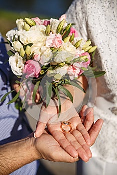 Hands of newlyweds with wedding rings lying on their palms and a wedding bouquet of flowers. Concept of wedding love and Valentine