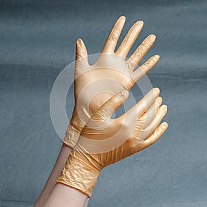 Hands in nitrile gloves of gold color on a gray background with a gradient