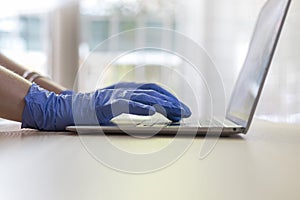 Hands with nitrile gloves typing on a laptop