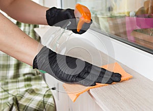 Hands in nitrile gloves wipe the surface of the window sill with detergent and an orange towel