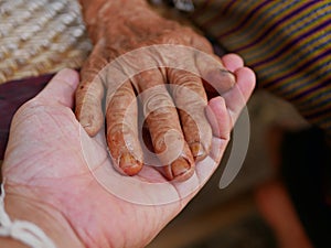 Hands of an old hard working woman on a hand of a younger man - care for elderly people