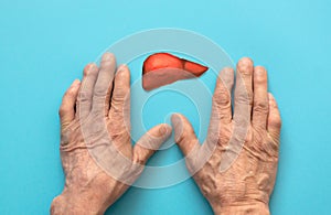 hands of an old man and a paper-cut liver symbol on a blue background. restoration of liver cells, hepatitis treatment,