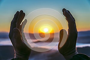 Hands of an old man reaching for the sun at sunrise, closeup. Concept of birth new life