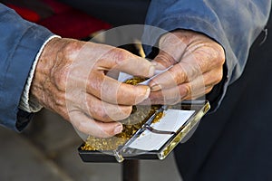 Hands of the old man are twisting tobacco cigarettes