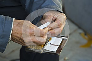 Hands of the old man are twisting tobacco cigarettes