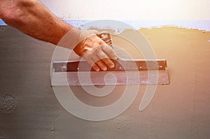 Hands of an old manual worker with wall plastering tools renovating house